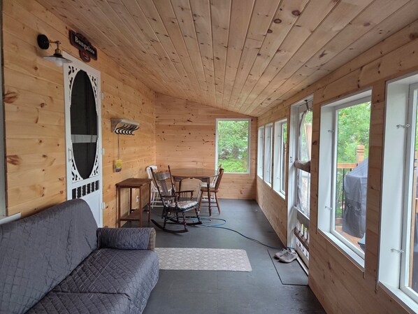 L’intérieur d’un chalet en bois, avec un canapé, des fauteuils à bascule, une table et de grandes fenêtres.