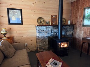 A cozy room with a stone fireplace, a sofa, a table with a notebook, and wooden walls.