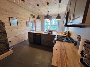 Una cocina con paredes de madera, una isla central, luces colgantes, una estufa y un fregadero.