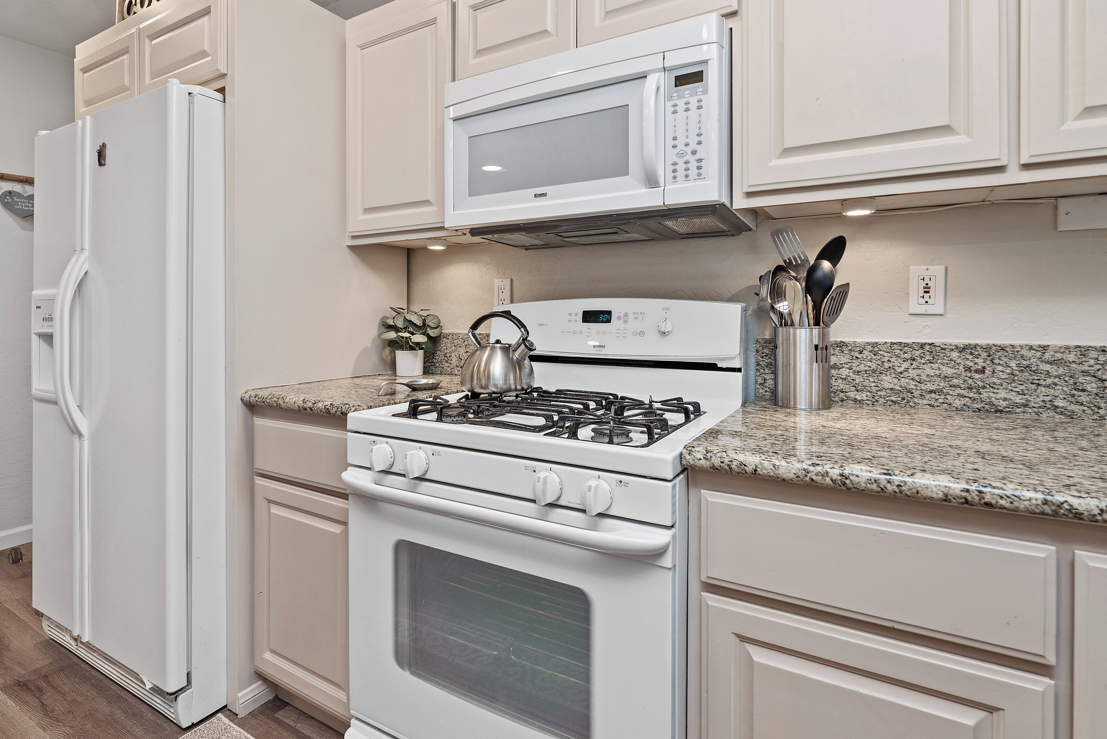 A kitchen with white appliances, granite countertops, and white cabinetry.