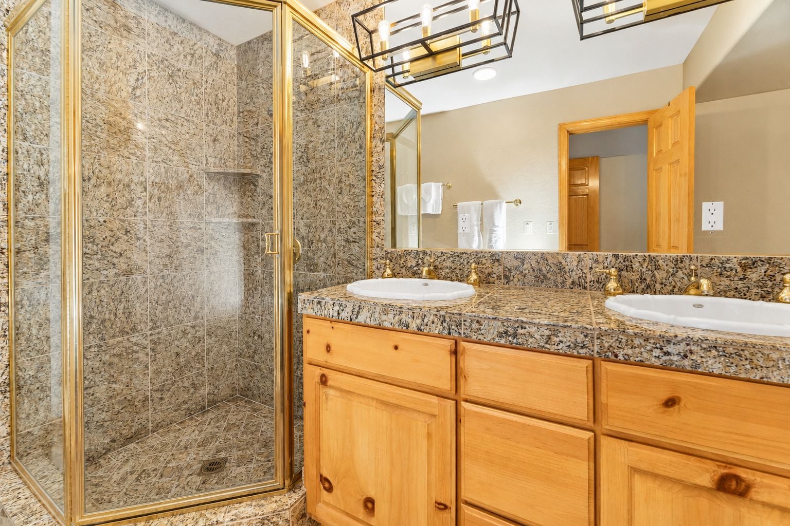 A bathroom with a walk-in shower, two sinks, wooden cabinets, and a large mirror.