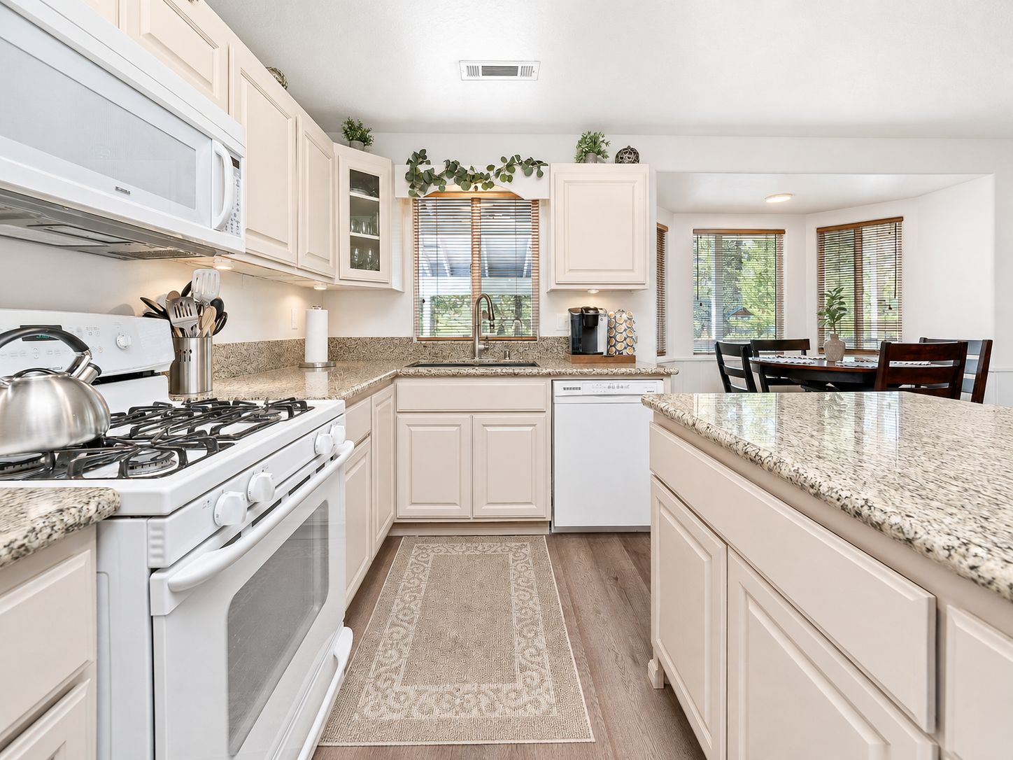 A kitchen with white cabinets, a stove, a dishwasher, and a dining area with a table and chairs.
