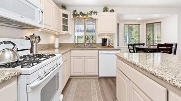 A kitchen with white cabinets, a stove, a dishwasher, and a dining area with a table and chairs.