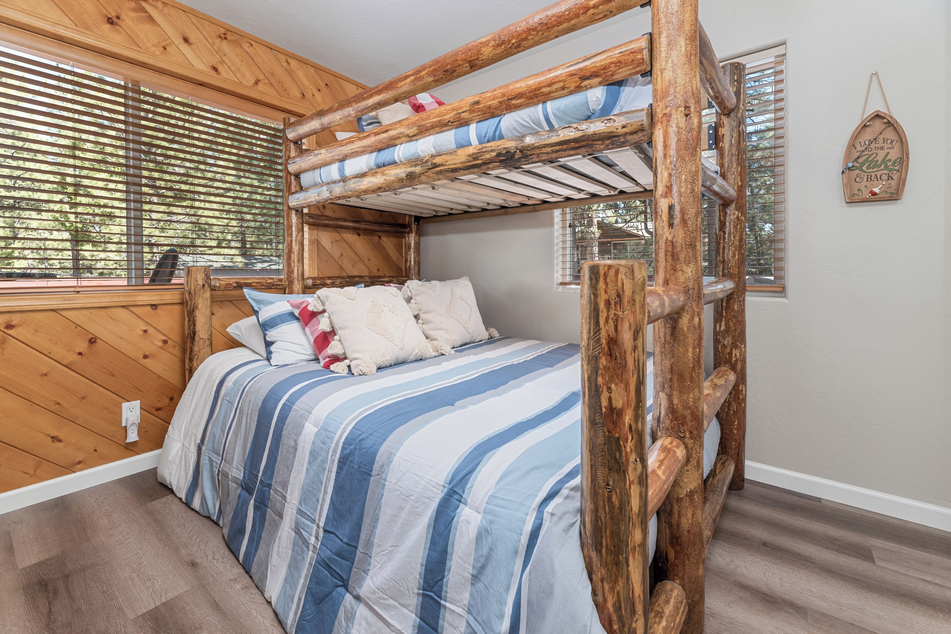 Een stapelbed met een houten frame, streepjesbeddengoed en een raam met zonwering.