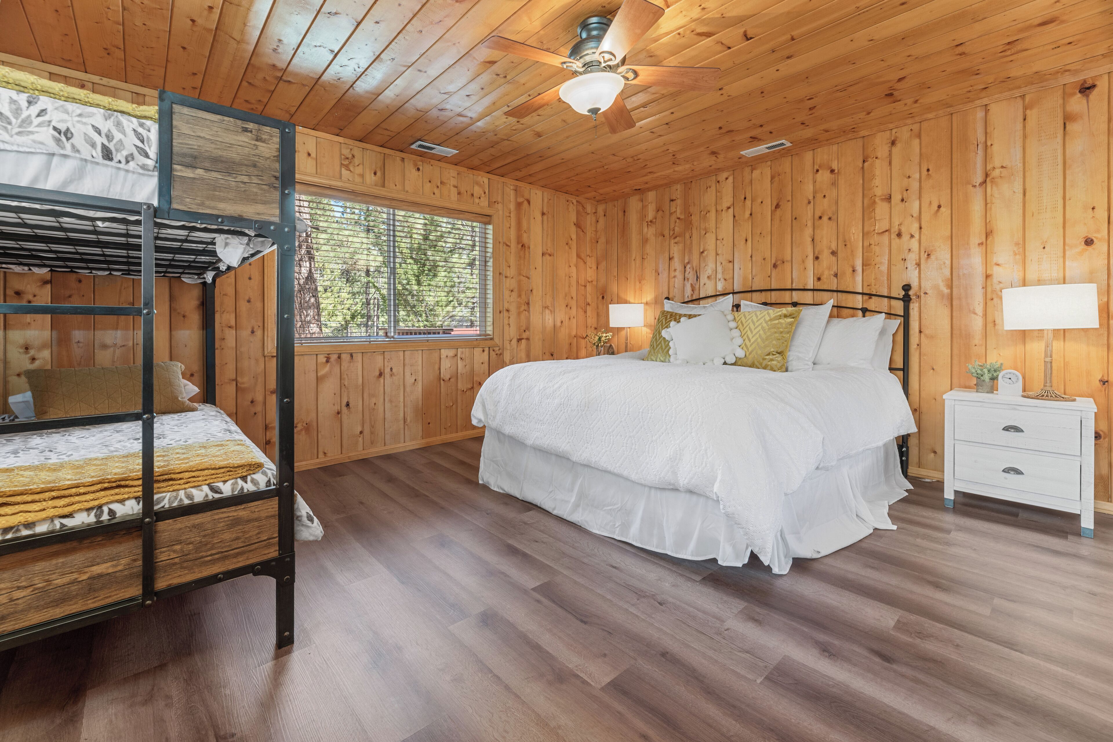 A wooden-paneled bedroom with a bunk bed, a single bed, a nightstand, and a ceiling fan.