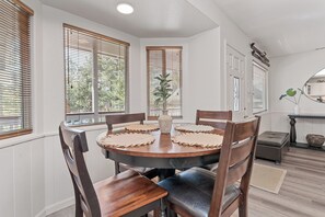A dining area with a round wooden table, six chairs, and a vase of flowers. - Serenity Knoll (Big Bear Lake)