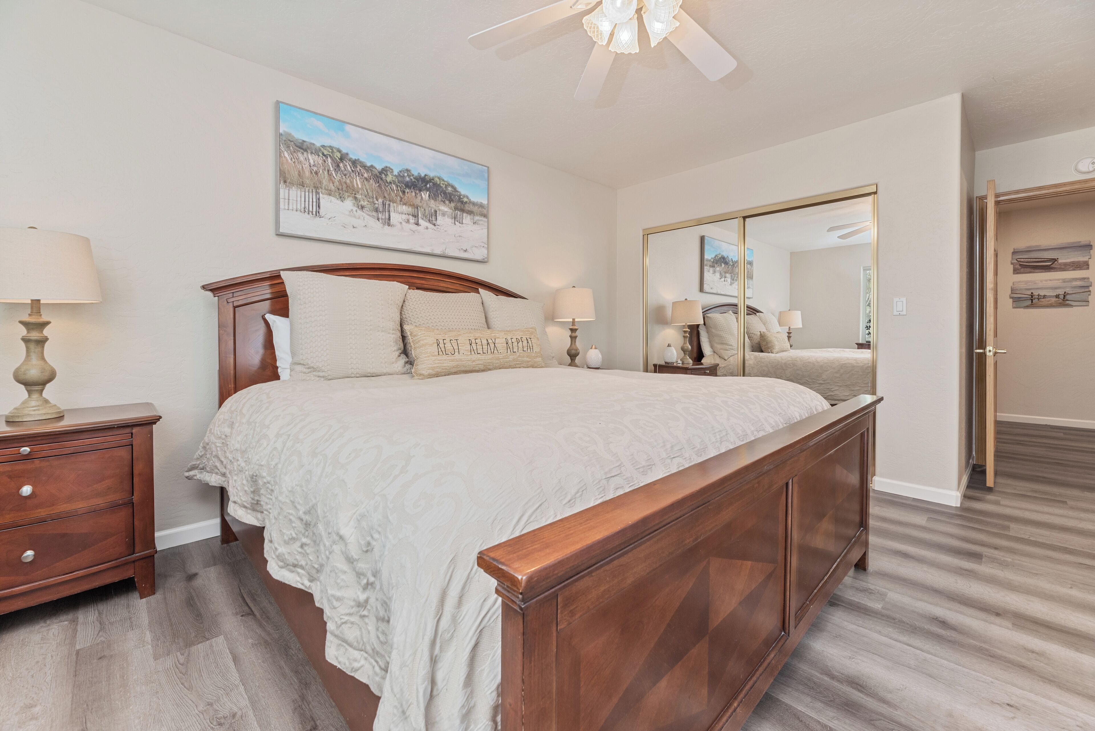 A bedroom with a wooden bed, two bedside tables with lamps, a large mirror, and a painting on the wall.