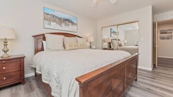 A bedroom with a wooden bed, two bedside tables with lamps, a large mirror, and a painting on the wall.