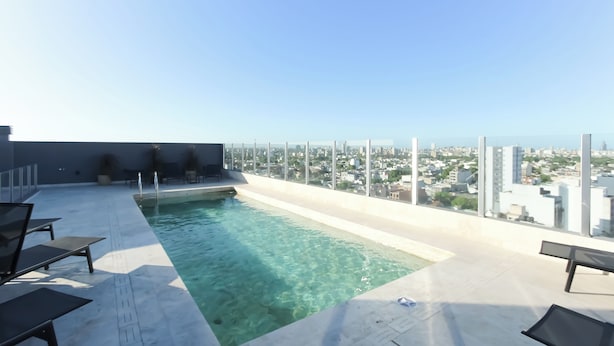 Ein Pool auf dem Dach mit klarem Wasser, umgeben von Liegestühlen und Blick auf die Stadt.