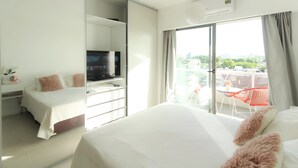 Ein Hotelzimmer mit einem Bett, einem Schreibtisch mit Fernseher und einem Balkon mit roten Stühlen.