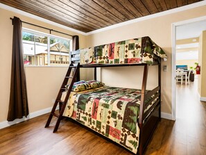 A bunk bed with a quilt, a wooden ladder, a window with curtains, and a view of a house outside. - Jaybird Lodge  (Big Bear Lake)