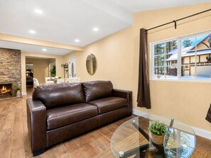 A living room with a leather sofa, a glass coffee table, and a fireplace. - Jaybird Lodge  (Big Bear Lake)