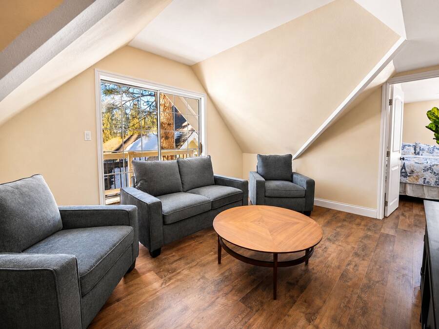 A loft-style room with a high ceiling, a wooden floor, a round coffee table, and two grey sofas.