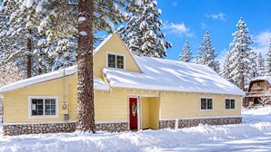 Um edifício de dois andares com uma porta vermelha, rodeado por árvores cobertas de neve.