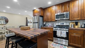 A modern kitchen with wooden cabinets, stainless steel appliances, and a wooden island with bar stools. - Jaybird Lodge  (Big Bear Lake)