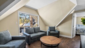 A loft-style living room with a high ceiling, a large window, and a view of a house. - Jaybird Lodge  (Big Bear Lake)