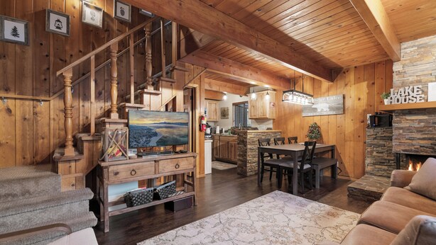 A wooden interior with a staircase, a fireplace, a dining area, and a television. - Shady Pine Cottage (Big Bear City)