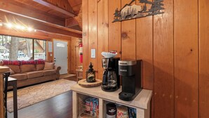 A cozy cabin interior with a wooden interior, a sofa, a coffee maker, and a shelf with books and a lantern. - Shady Pine Cottage (Big Bear City)