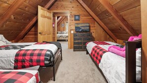 A cozy attic bedroom with two beds, a dresser, and a television. - Shady Pine Cottage (Big Bear City)