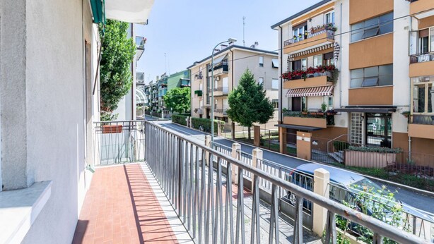 A residential street with multi-story buildings, balconies with flower boxes, and a clear sky.