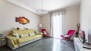 A living room with a sofa, two chairs, a TV, and a painting on the wall.