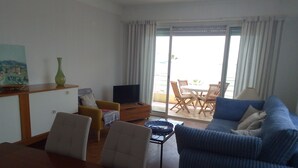 A living room with a sofa, chairs, a TV, a table, and a balcony with a table and chairs.