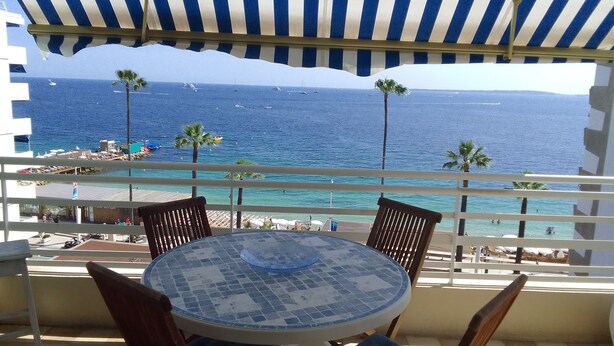 A balcony with a view of the ocean, a tiled table, and wooden chairs.
