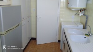 A compact kitchen with a refrigerator, a microwave, a sink, and a door leading to another room.