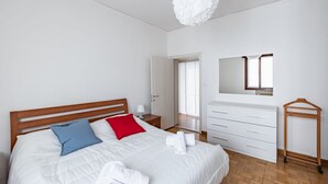 A bedroom with a bed, bedside table, dresser, and a hanging light fixture.