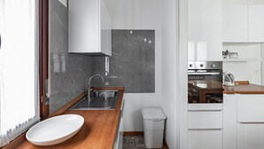 A compact kitchen with a sink, a white cabinet, and a small trash bin.
