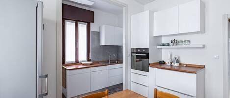 Een koelkast, een oven, een kookplaat, kookgerei, borden en bestek