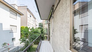 A narrow balcony with a metal railing, a tiled floor, and a view of adjacent buildings and greenery.