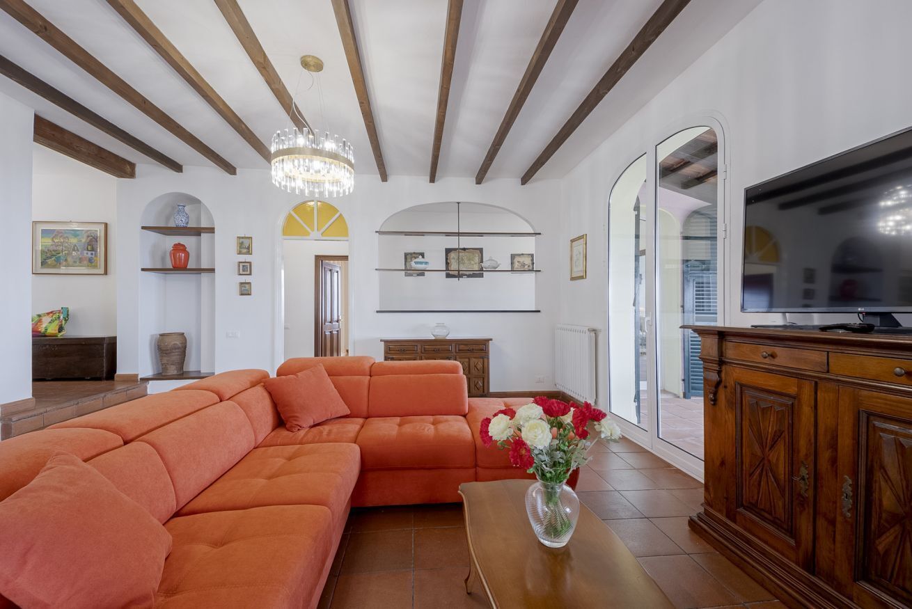 A living room with a sectional sofa, a wooden cabinet, a television, and a chandelier.