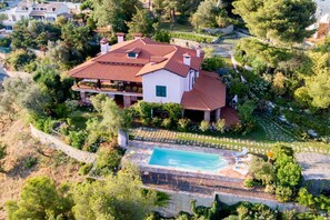 A large house with a swimming pool, surrounded by lush greenery and a stone wall.