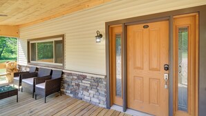 A covered porch with wicker furniture, a stone wall, and a wooden door with a keypad lock. - Champion Vacation Rental with Fire Pit! (Champion)