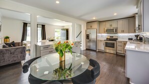 Una cocina moderna con electrodomésticos de acero inoxidable, un comedor con mesa de vidrio y una sala de estar con sofá y planta.