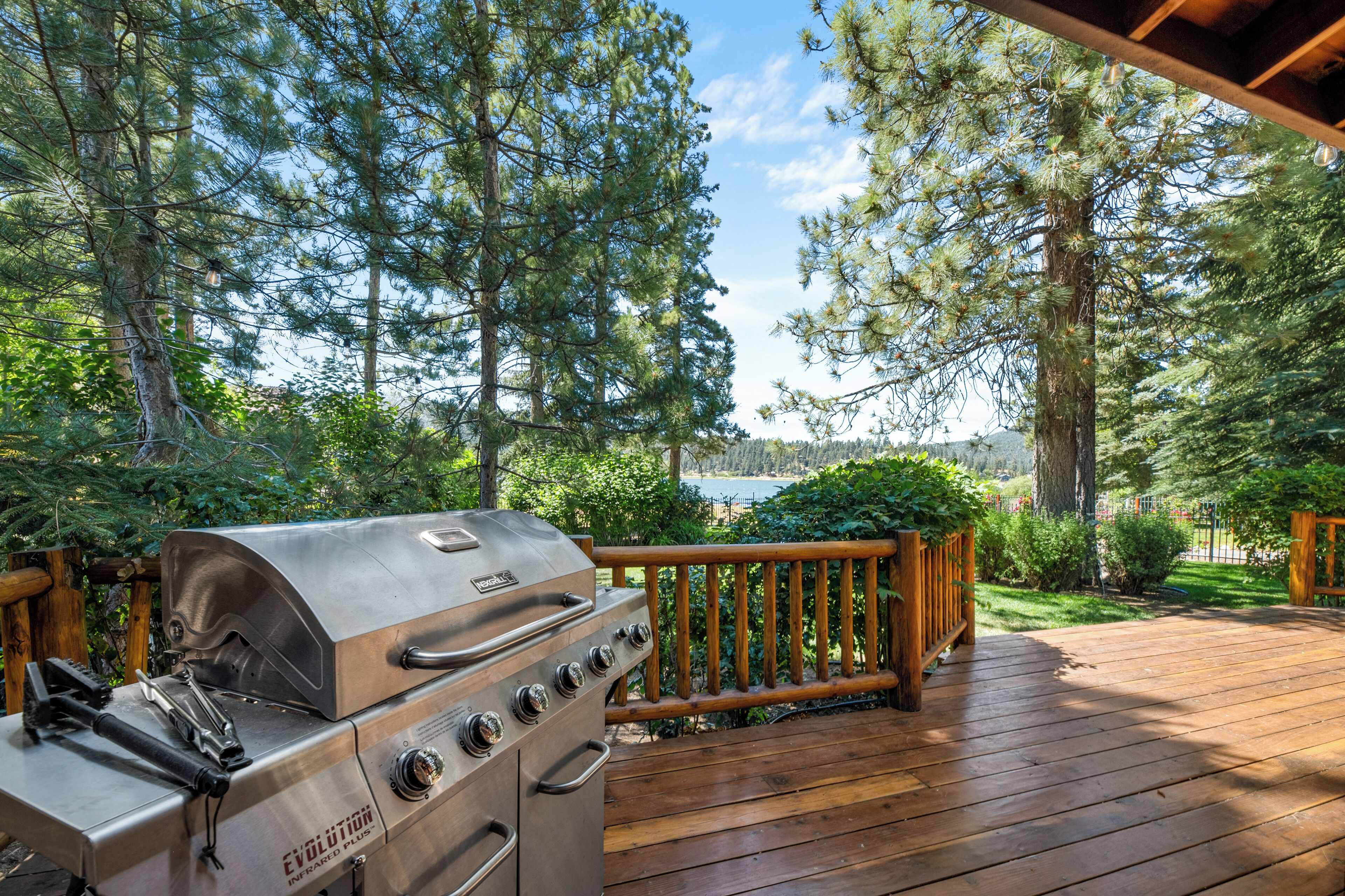 Un barbecue installé sur une terrasse en bois, avec vue sur des arbres et un lac.