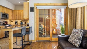 Una cocina moderna con armarios de madera, microondas integrado y estufa a gas. Hay un comedor con mesa y sillas, y una sala de estar con sofá y un cojín decorativo.