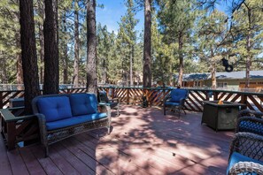 A wooden deck with wicker furniture, a fire pit, and a view of tall pine trees.