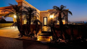 A modern house with a well-lit entrance, palm trees, and a view of the ocean. - 25% Off Sept 7-9, Amazing Reviews/Views, Hot Tub! (Ventura)