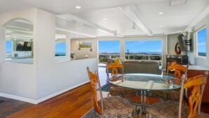A dining area with a glass table and chairs, large windows with a view, and a modern ceiling design. - 25% Off Sept 7-9, Amazing Reviews/Views, Hot Tub! (Ventura)