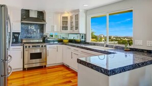 A modern kitchen with white cabinets, a stainless steel stove, and a large window offering a city view. - 25% Off Sept 7-9, Amazing Reviews/Views, Hot Tub! (Ventura)