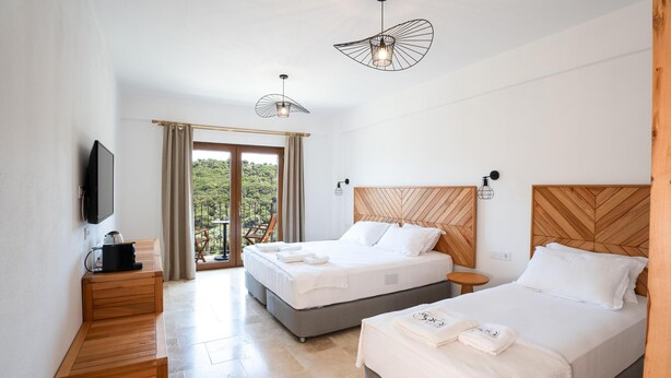 Habitación de hotel con dos camas, un televisor, un banco de madera y un balcón con vistas a zonas verdes.