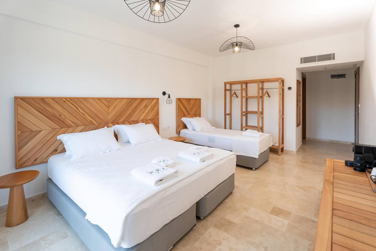A hotel room with two beds, a wooden headboard, a small round table, and a wooden desk with a chair.