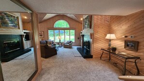 Uma sala de estar aconchegante com lareira, um sofá e uma mesa de centro. Há uma janela grande que oferece luz natural e vista para o exterior.