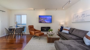 Uma sala de estar moderna com área de jantar, uma televisão grande e uma obra de arte com tema praiano.