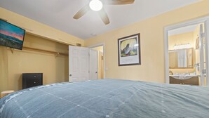 A bedroom with a bed, a ceiling fan, a door, a framed picture, and a bathroom visible through an open door. - Irie's Retreat (Sugarloaf)