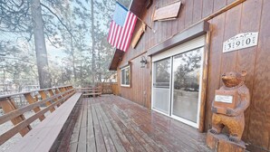 A wooden deck with a wooden bench, an American flag, a bear sculpture, and a sliding glass door. - Irie's Retreat (Sugarloaf)
