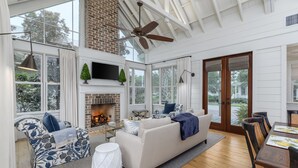 Un salón amplio con chimenea, ventilador de techo y ventanas grandes.