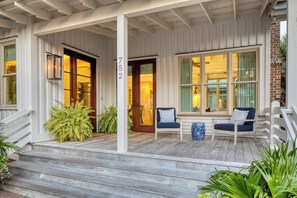 A porch with wooden steps, two chairs, and a large potted plant. - Stylish Cottage with brick courtyard + outdoor fireplace (Bluffton)